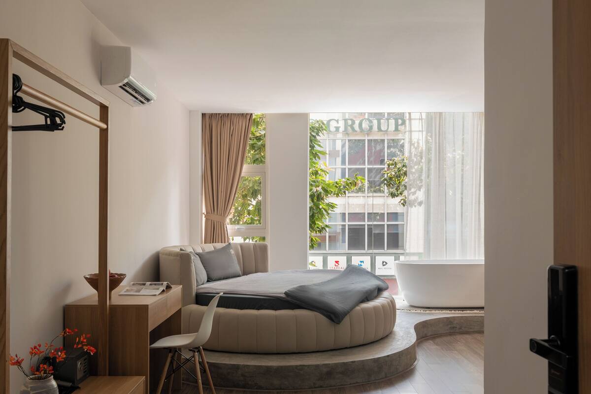 Ein modernes Schlafzimmer mit einem gebogenen Bett, einem Schreibtisch und einem großen Fenster mit Vorhängen.