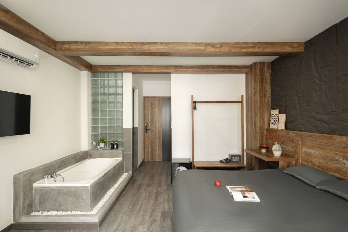 Ein modernes Schlafzimmer mit einem großen Bett, einem Holz-Kopfteil, einer integrierten Badewanne und einem kleinen Nachttisch mit einer Vase.