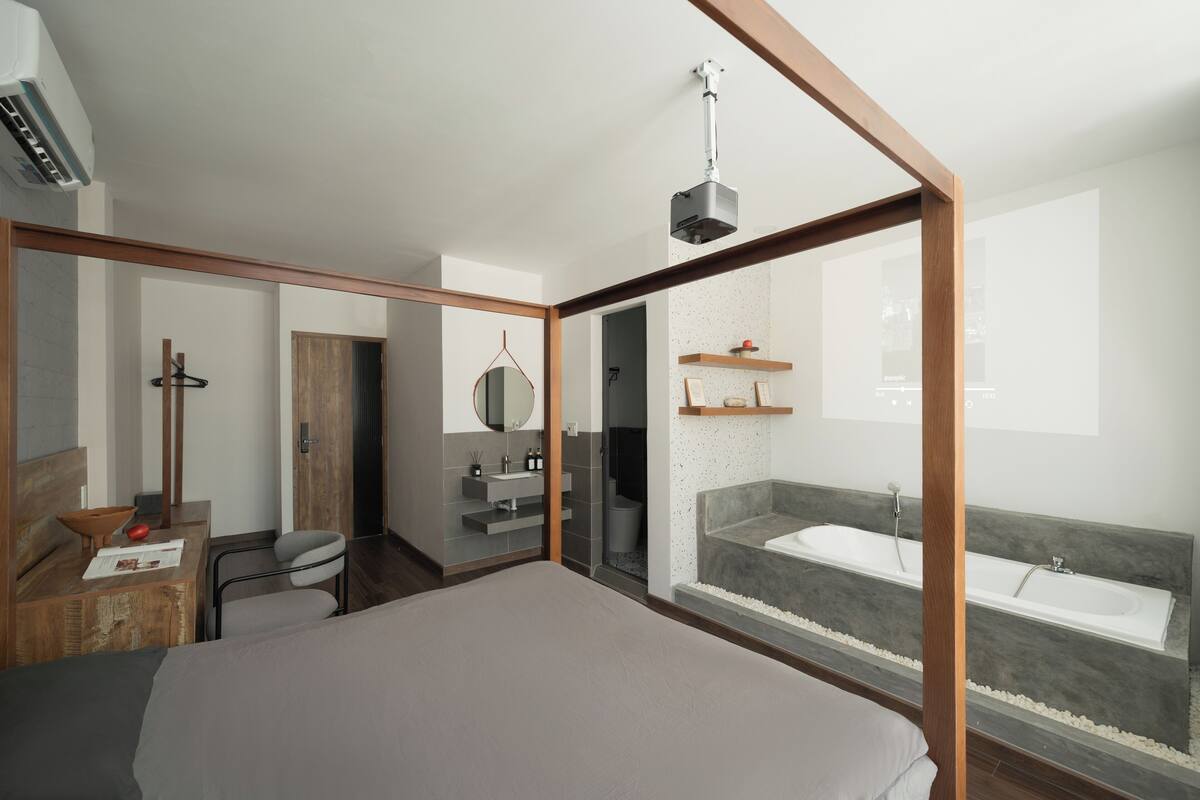 Ein modernes Schlafzimmer mit einem großen Bett, einem Schreibtisch, einem Stuhl, einem Spiegel, einem Frisiertisch mit Waschbecken und einer Badewanne.