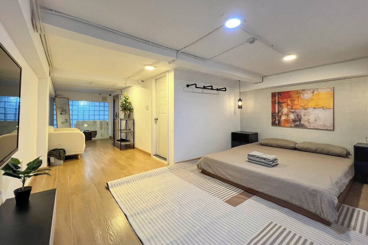 Ein modernes Schlafzimmer mit einem großen Bett, einem Schreibtisch und einem Stuhl. Auf dem Schreibtisch steht eine Pflanze und an der Wand hängt ein Gemälde.