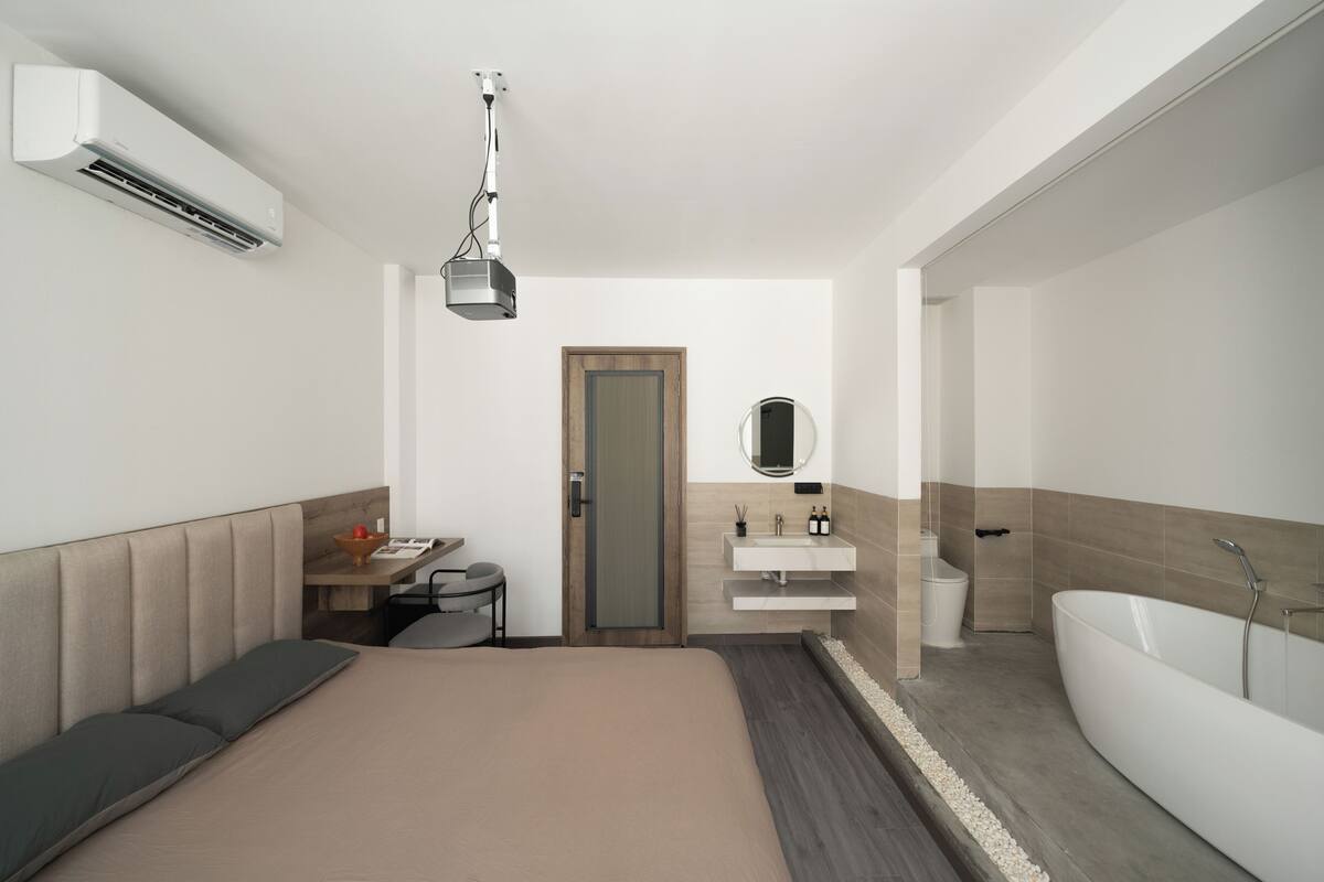 Ein modernes Hotelzimmer mit Bett, Nachttisch, Klimaanlage und einem Badezimmer mit Badewanne und Waschbecken.