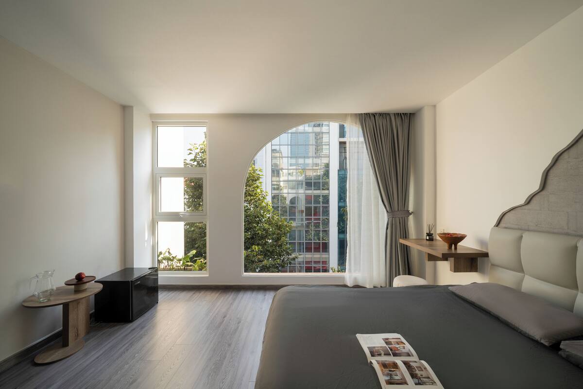 Ein modernes Schlafzimmer mit großem Fenster, einem Bett mit Zeitschrift, einem kleinen Tisch mit Glas und einem Nachttisch mit Lampe.