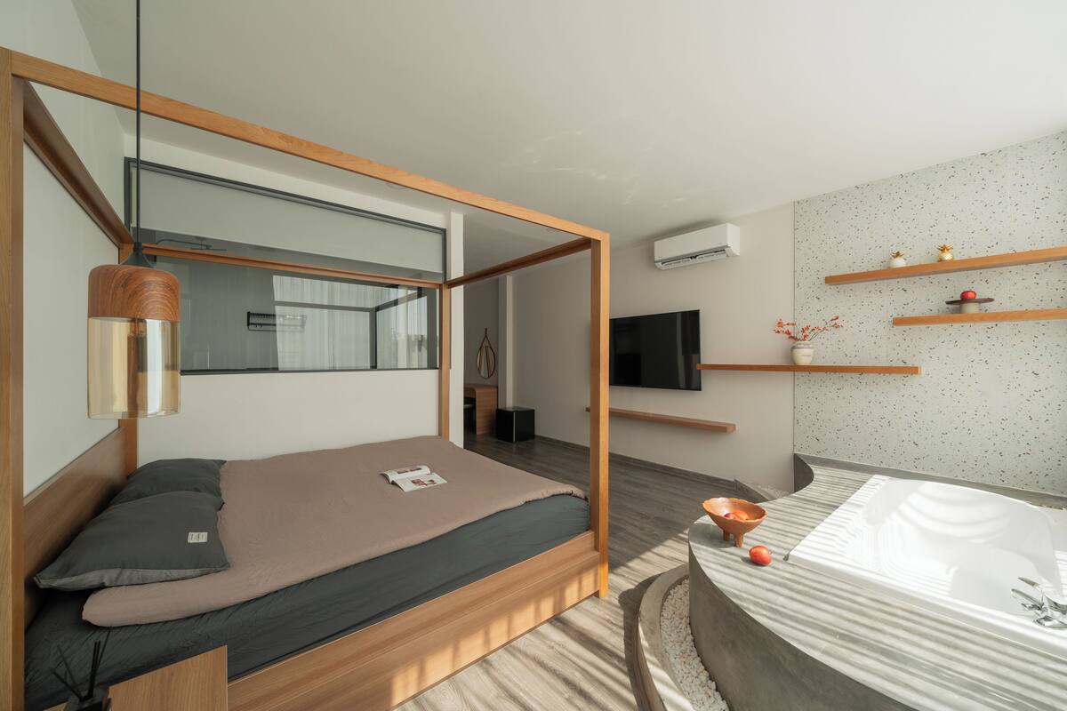 Ein modernes Schlafzimmer mit Holzbettgestell, Nachttisch, Fernseher und einem Badezimmer mit Badewanne.
