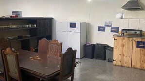 Zona pranzo con tavolo e sedie in legno, angolo cottura con mobili e elettrodomestici, e un cestino per i rifiuti.