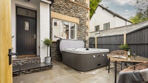 A stone house with a black door marked '3', a hot tub, wicker chairs, and a small table with a book and glasses. - Ferry View Cottage in Bowness-on-windermere (Windermere)