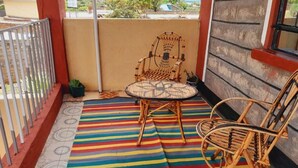 Un balcon avec un tapis à rayures, deux fauteuils en osier et une vue sur l’extérieur.