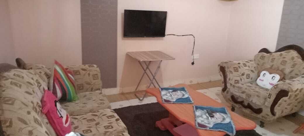 A living room with two patterned sofas, a small table, and a television mounted on the wall.