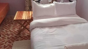 Un lit avec une literie blanche, une table de chevet en bois et un sol à motifs.