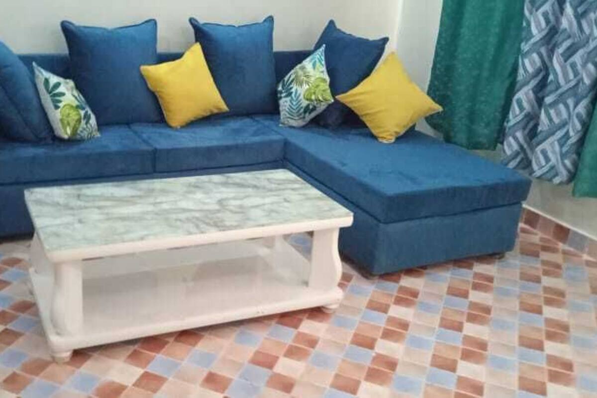 Una sala de estar con un sofá azul, una mesa de centro blanca y cortinas estampadas.