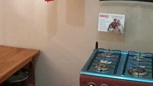 Une cuisine équipée d’une cuisinière à gaz, d’étagères remplies d’ustensiles de cuisine, d’une bouteille de gaz rouge et d’une serviette bleue accrochée au mur.