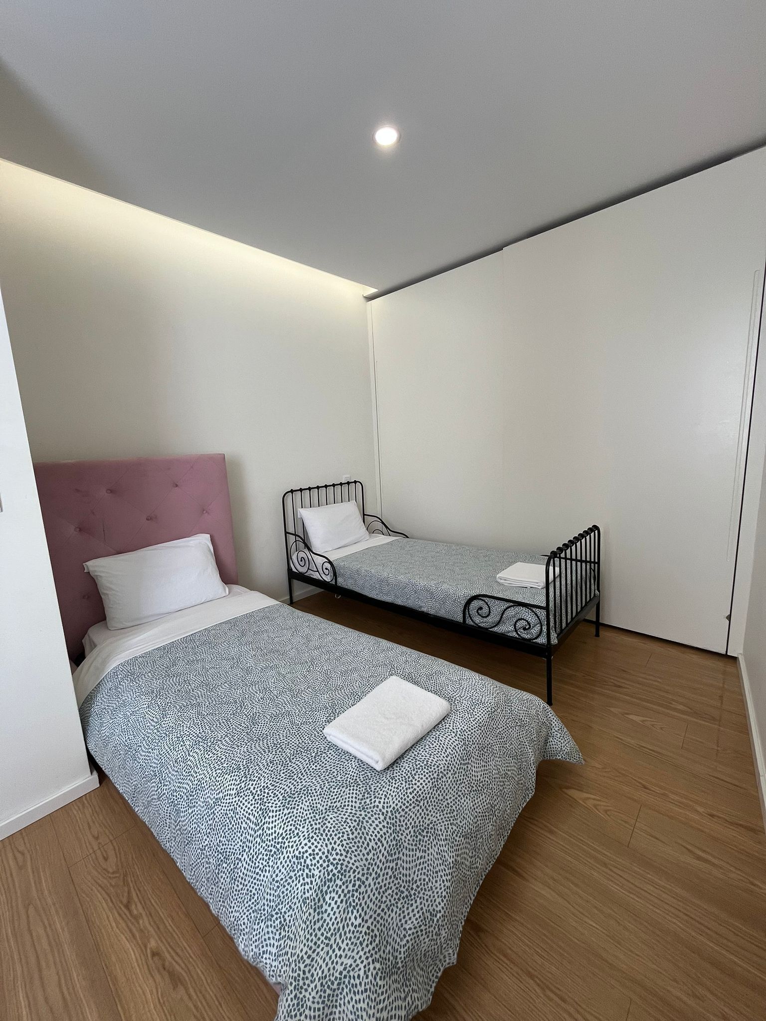 Una habitación pequeña y moderna con dos camas, un cabecero rosa y una lámpara en el techo.