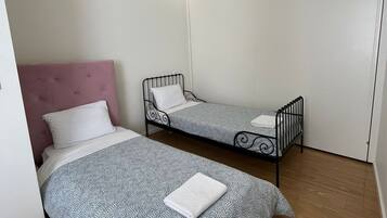 Una habitación pequeña y moderna con dos camas, un cabecero rosa y una lámpara en el techo.