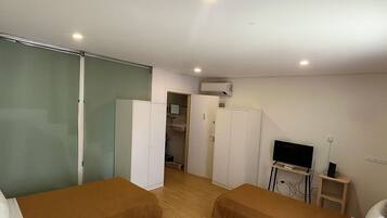 Habitación de hotel con dos camas, televisor, armario y baño visible a través de una puerta abierta.