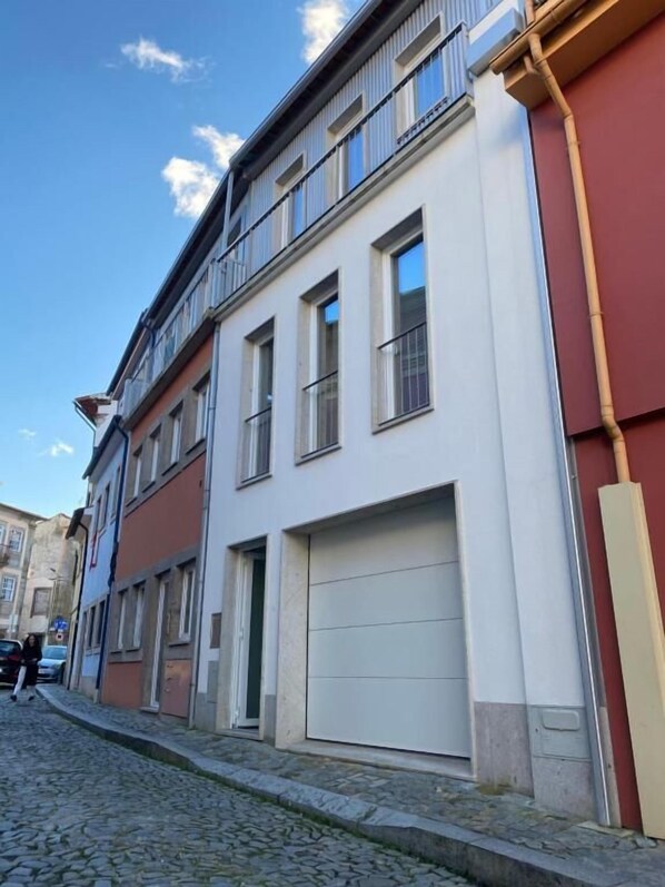 A multi-story building with a white facade and a red section on the right. There is a visible garage door on the ground floor. - Casa Augusta 4 (Braga)