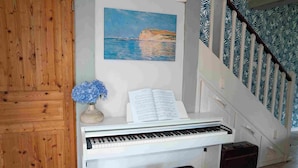 Ett piano med noter, en vas med blommor och en målning som föreställer ett kustlandskap.