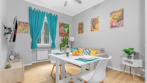 Ein moderner Essbereich mit einem weißen Tisch, blauen Vorhängen und farbenfroher Kunst an den Wänden.