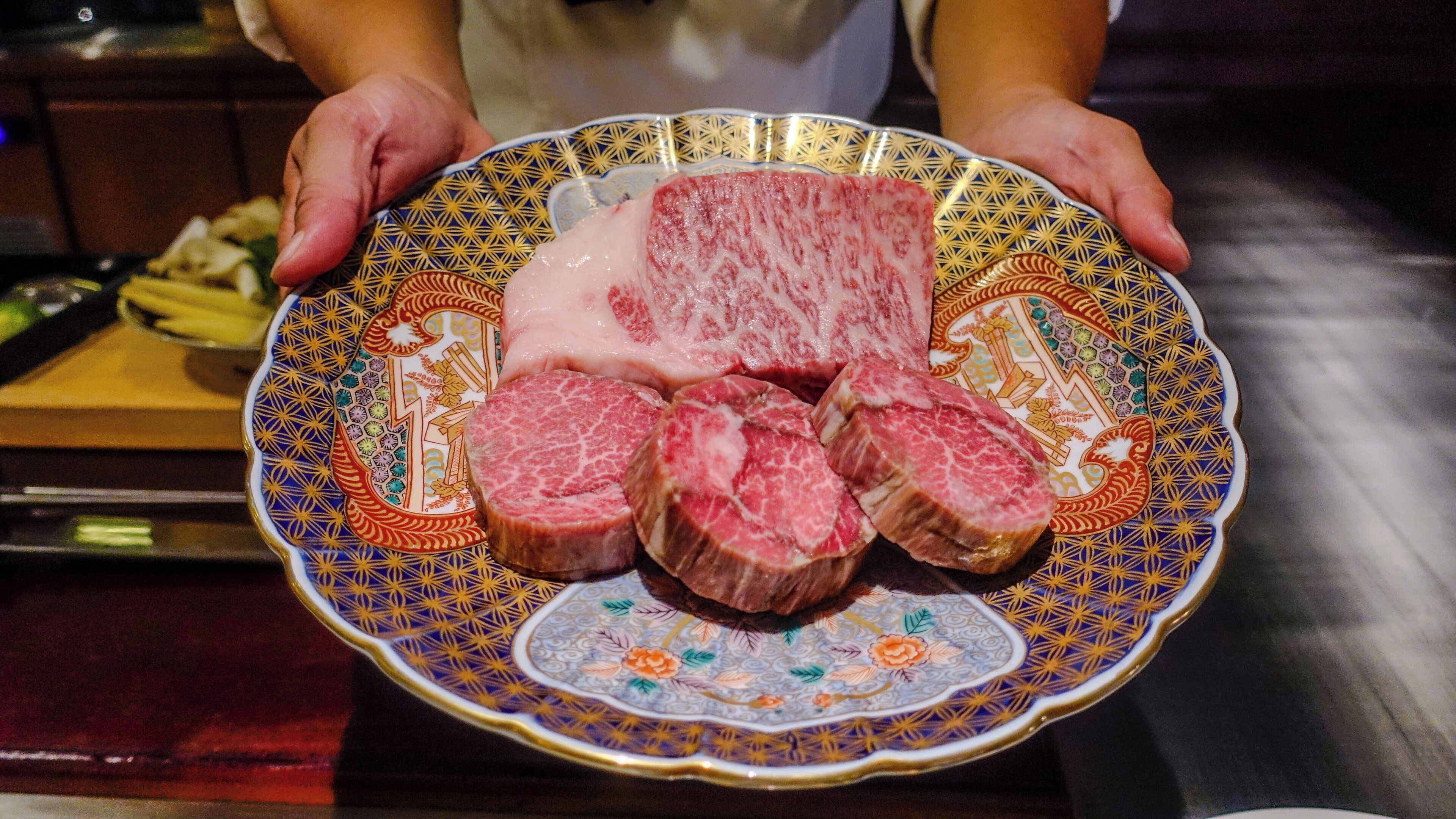 A person holding a decorative plate with sliced meat.