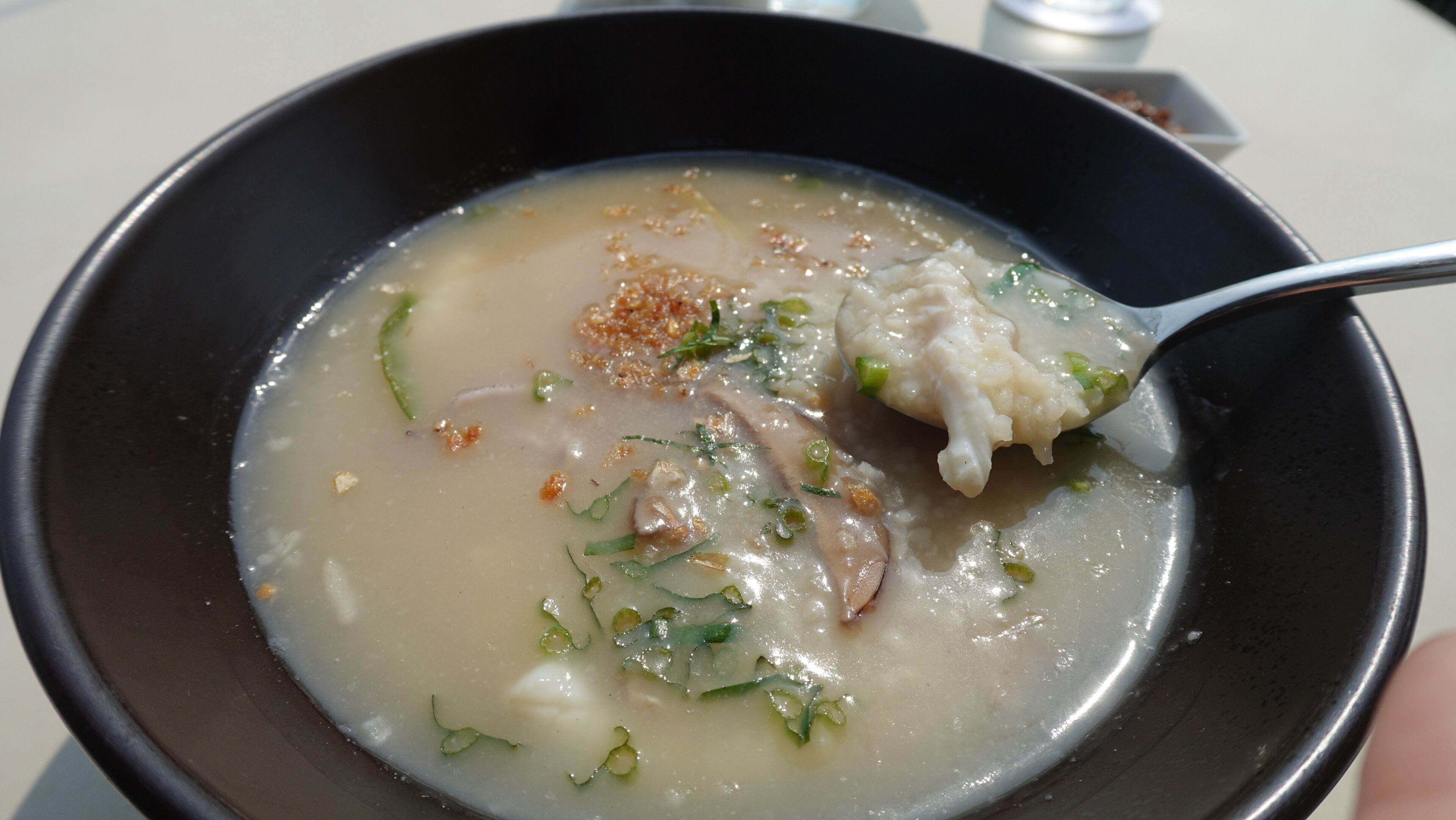A bowl of soup with a spoon, containing a clear broth, pieces of meat, and green herbs.