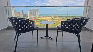 Un balcón con dos sillas y una pequeña mesa, con vistas a un paisaje urbano y una masa de agua.