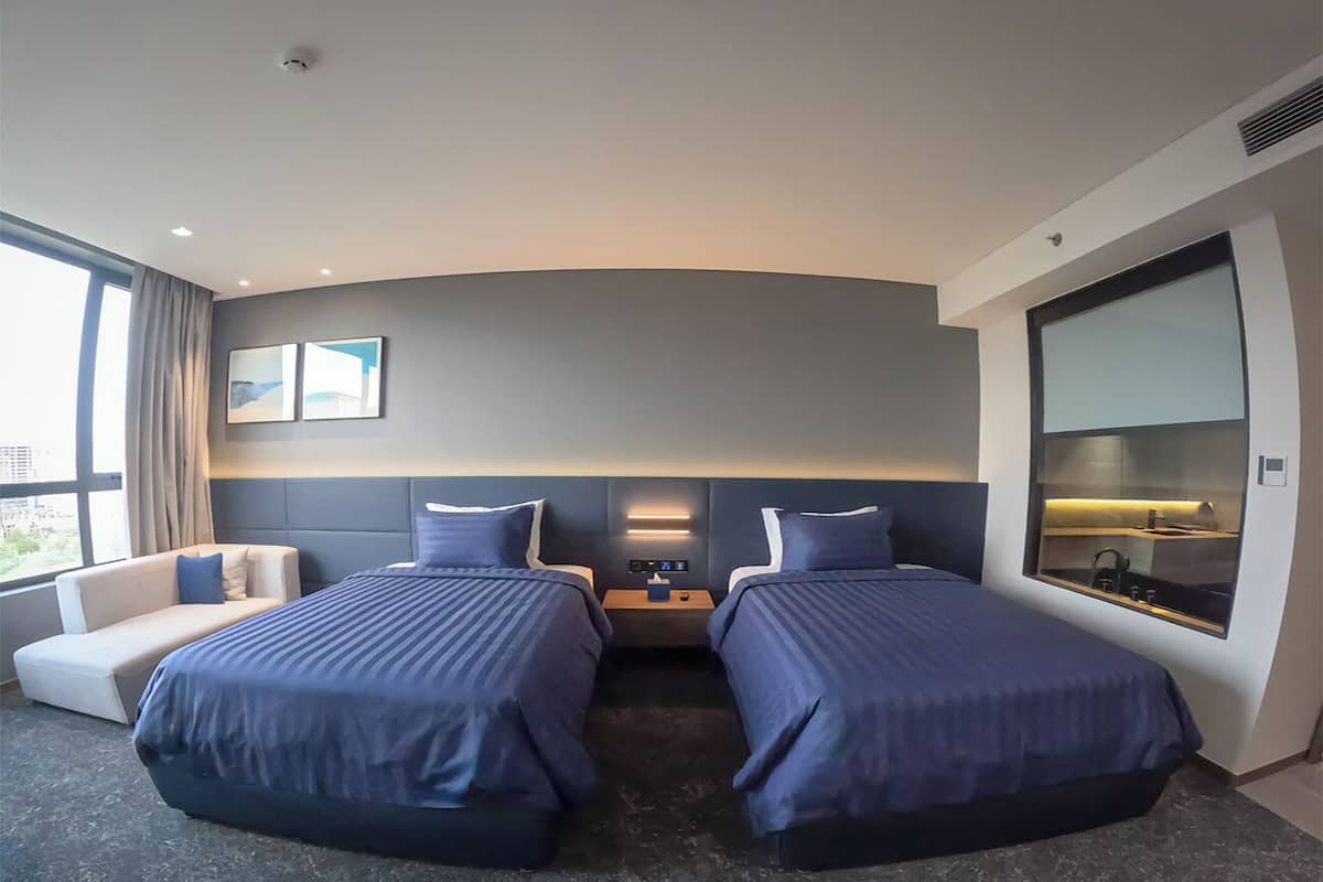 Ein Hotelzimmer mit zwei Betten, einem Sofa, einem Nachttisch, einem großen Fenster und einem Spiegel.