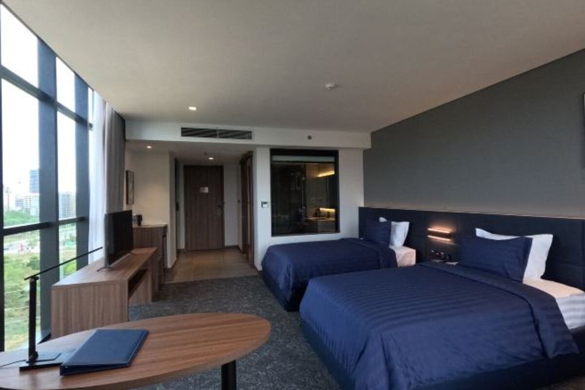A hotel room with two beds, a desk, a chair, and a large window.