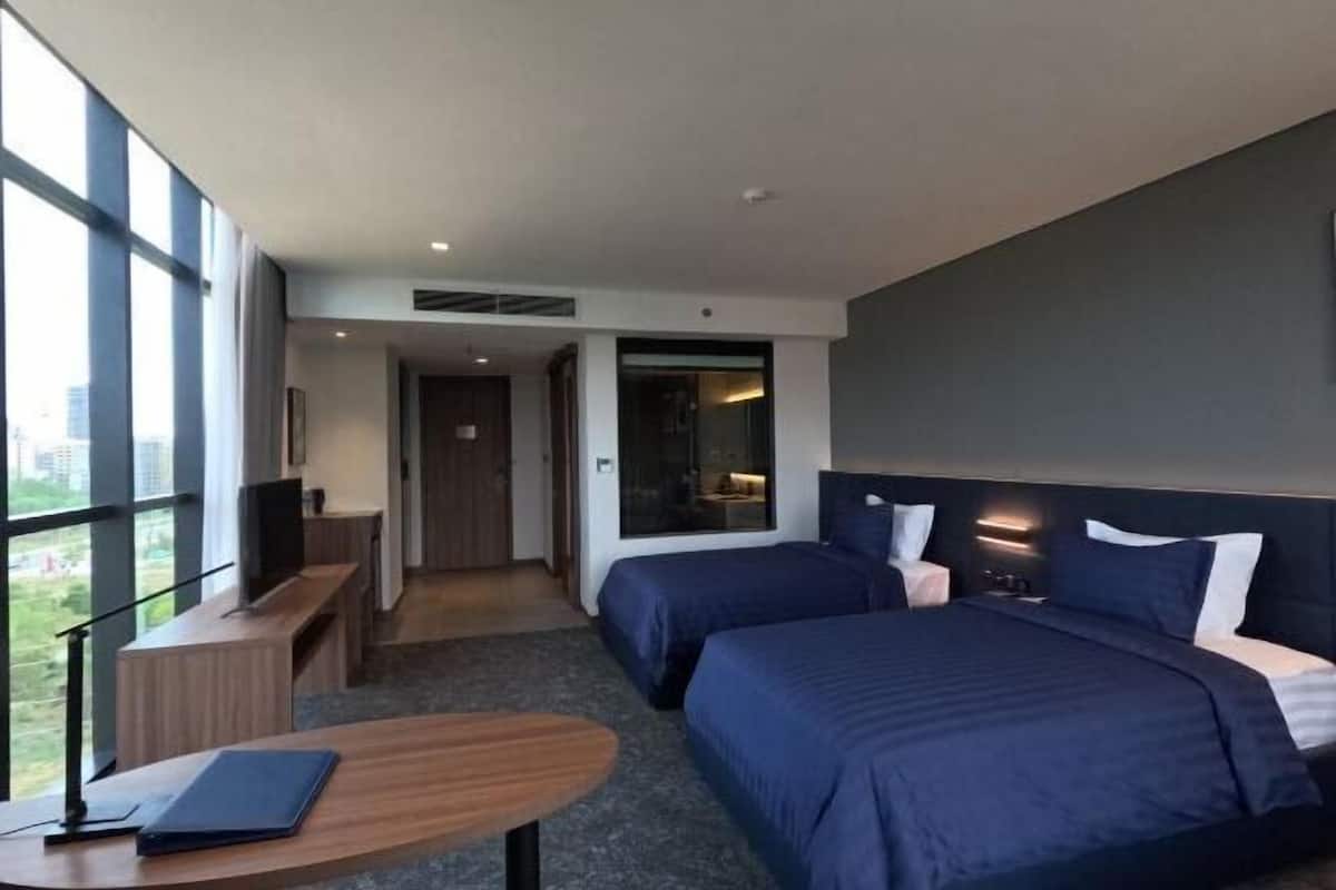 Ein Hotelzimmer mit zwei Betten, einem Schreibtisch, einem Sessel und einem großen Fenster.