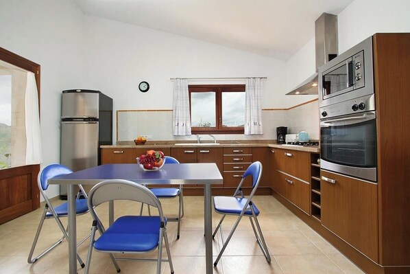 A compact kitchen with a dining table, chairs, a refrigerator, a stove, and a clock on the wall. - Finca MARA,  Pool, view, quiet location, 3 bedrooms A/C, 2 bathrooms, WIFI (IB)