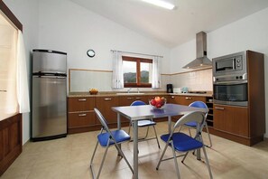 A compact kitchen with a refrigerator, oven, and microwave. There is a dining table with chairs and a window with curtains. - Finca MARA,  Pool, view, quiet location, 3 bedrooms A/C, 2 bathrooms, WIFI (IB)