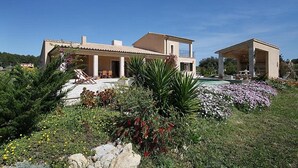 Una casa de dos pisos con piscina, rodeada de abundante vegetación y diversas plantas.