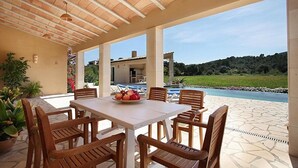 Un patio al aire libre con una mesa, sillas, una piscina y vistas a una casa y paisaje.