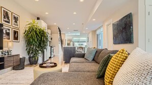 A modern living room with a sofa, a large potted plant, and a kitchen in the background. - NEW BUILD Pet Friendly I Highlands I RiNo I Dwntwn (Denver)
