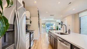 A modern kitchen with stainless steel appliances, a central island with a sink, and a view into the dining area. - NEW BUILD Pet Friendly I Highlands I RiNo I Dwntwn (Denver)