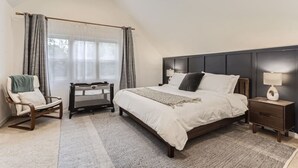Een slaapkamer met een groot bed, een nachtkastje met een lamp, een stoel en een ledikant.