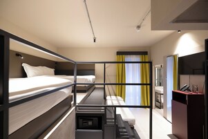 A modern hotel room with bunk beds, a desk, and a small kitchenette.