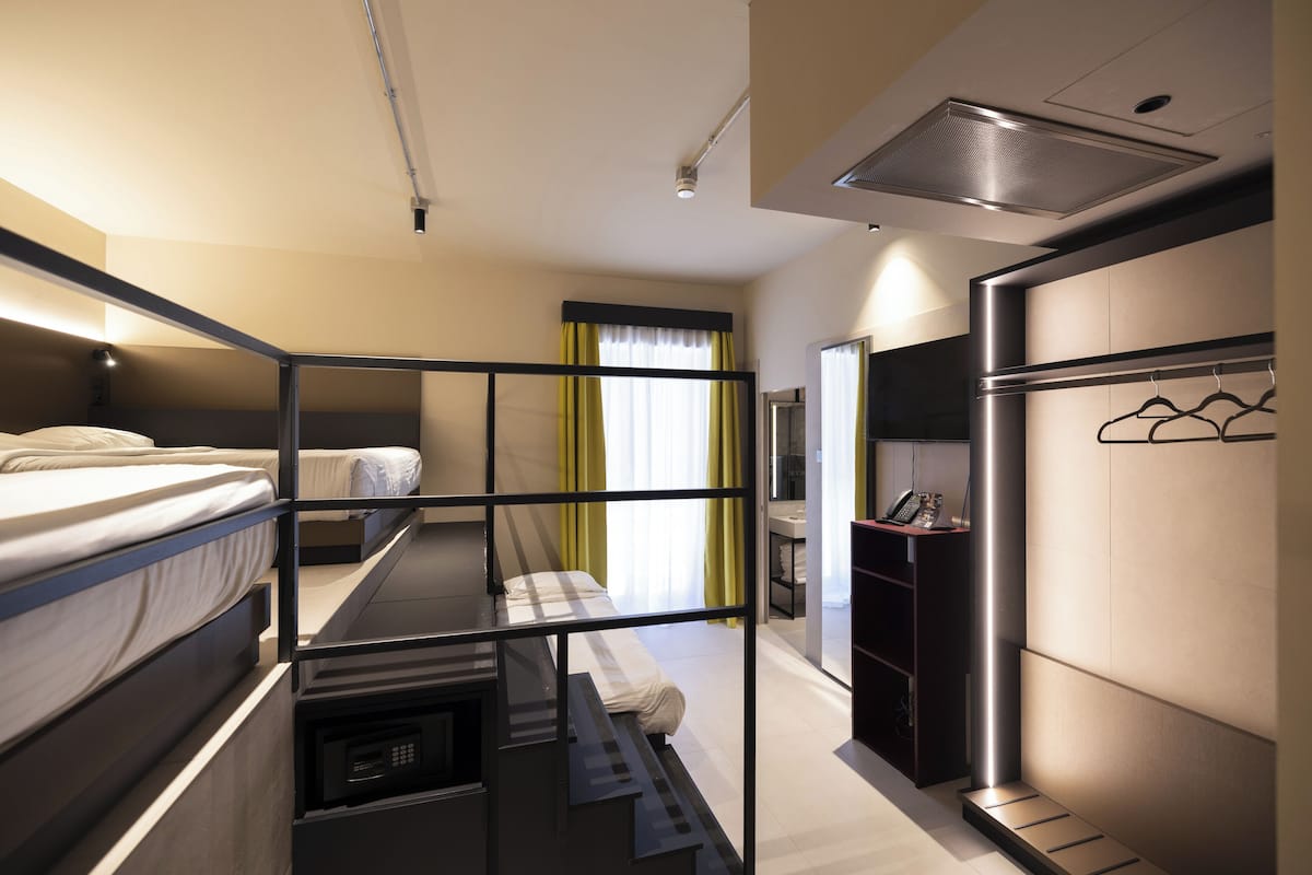 A hotel room with bunk beds, a desk, a wardrobe, and a bathroom visible through an open door.
