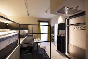 Een hotelkamer met stapelbedden, een bureau, een kledingkast en een badkamer zichtbaar door een geopende deur.