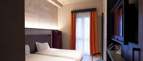 Habitación de hotel con dos camas, un escritorio, una silla, un televisor y una ventana con cortinas naranjas.