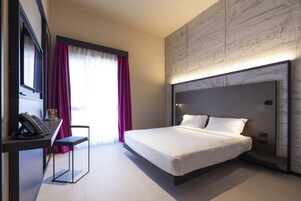 Una moderna camera d'hotel con un ampio letto, una scrivania con il telefono e una sedia.