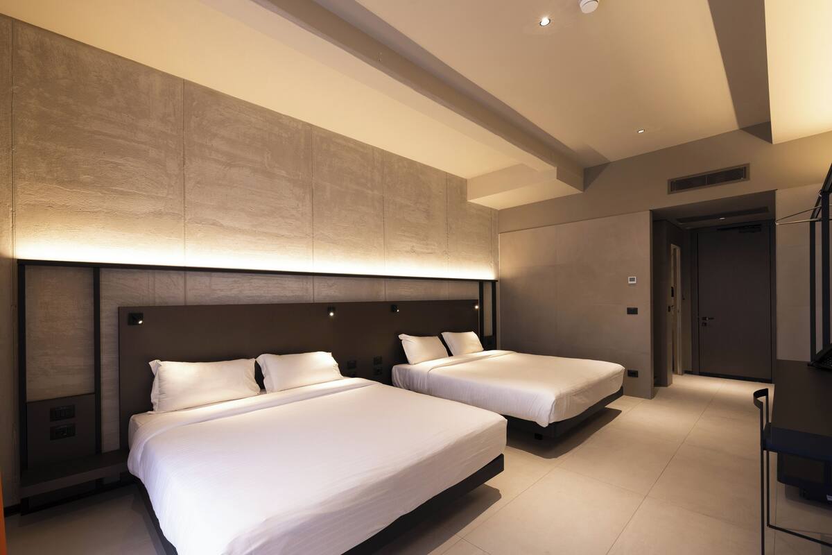 A modern hotel room with two beds, a desk, and a large wall-mounted light fixture.