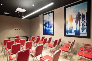 Una sala conferenze con sedie rosse e uno schermo per proiezioni.