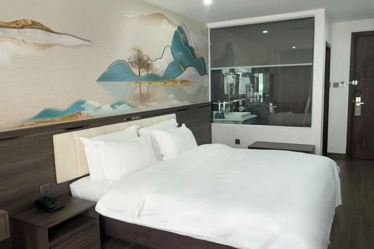 A modern hotel room with a large bed, a nightstand, a mirror, and a wall mural.