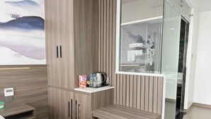 Ein modernes Hotelzimmer mit einem Holzschrank, einem kleinen Tisch mit Toilettenartikeln, einer Bank und einer Dusche mit Glasabtrennung.