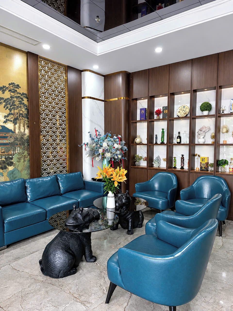 A modern living room with a blue sofa set, a coffee table with decorative items, and a bookshelf with various objects.