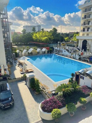 A swimming pool with lounge chairs and umbrellas, surrounded by potted plants and a car.