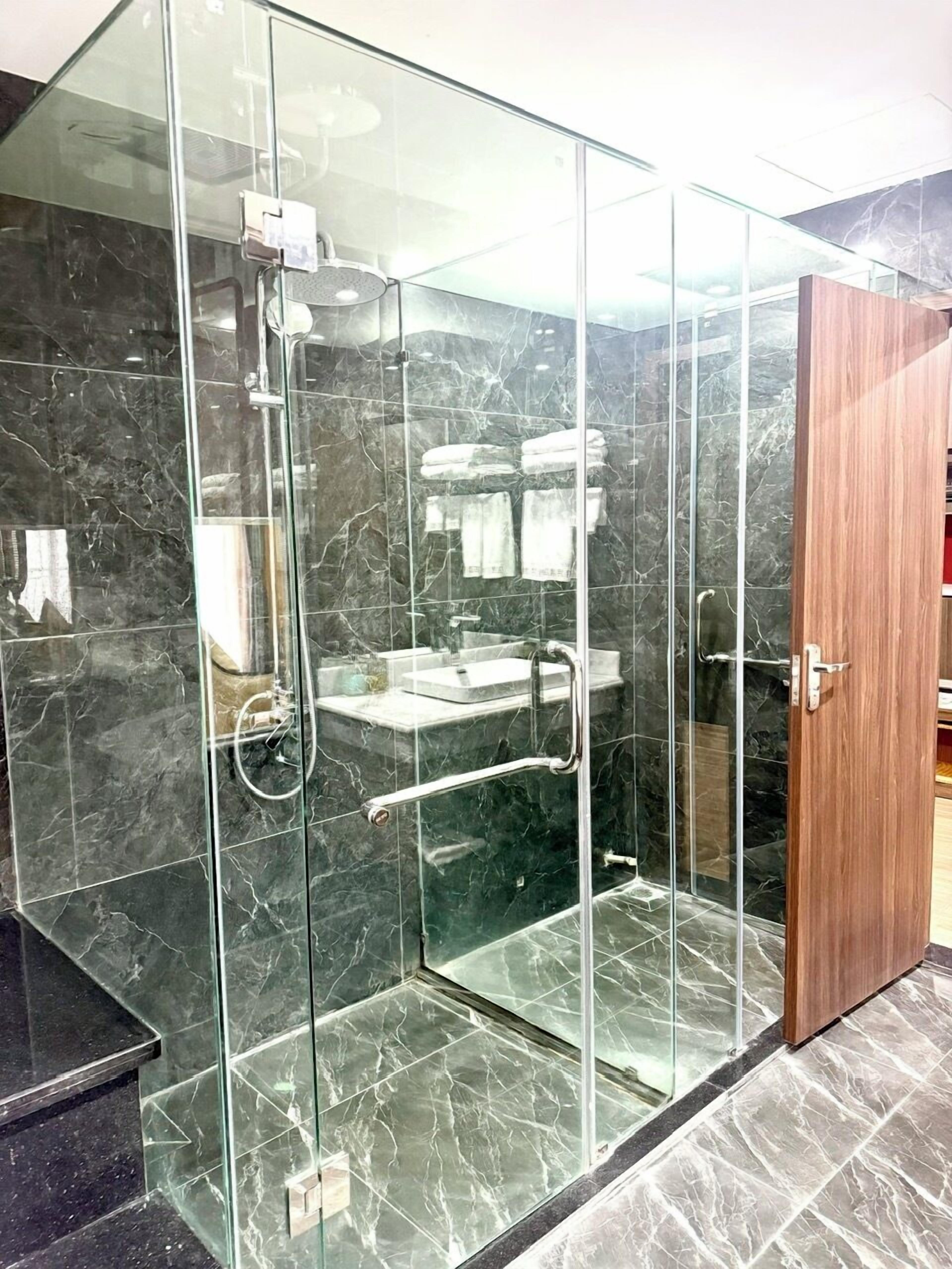Un baño moderno con cabina de ducha de vidrio, baldosas de mármol y puerta de madera.