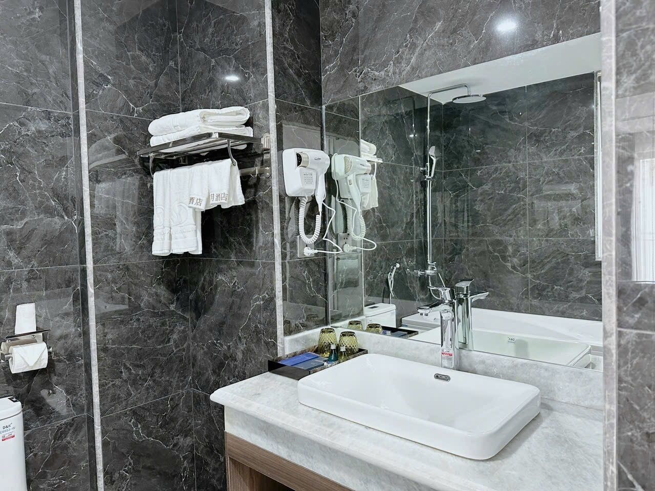 Un baño moderno con pared de mármol, un espejo grande, un lavamanos blanco y una zona de ducha.
