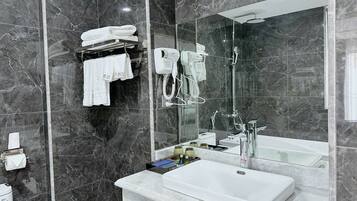 Un baño moderno con pared de mármol, un espejo grande, un lavamanos blanco y una zona de ducha.