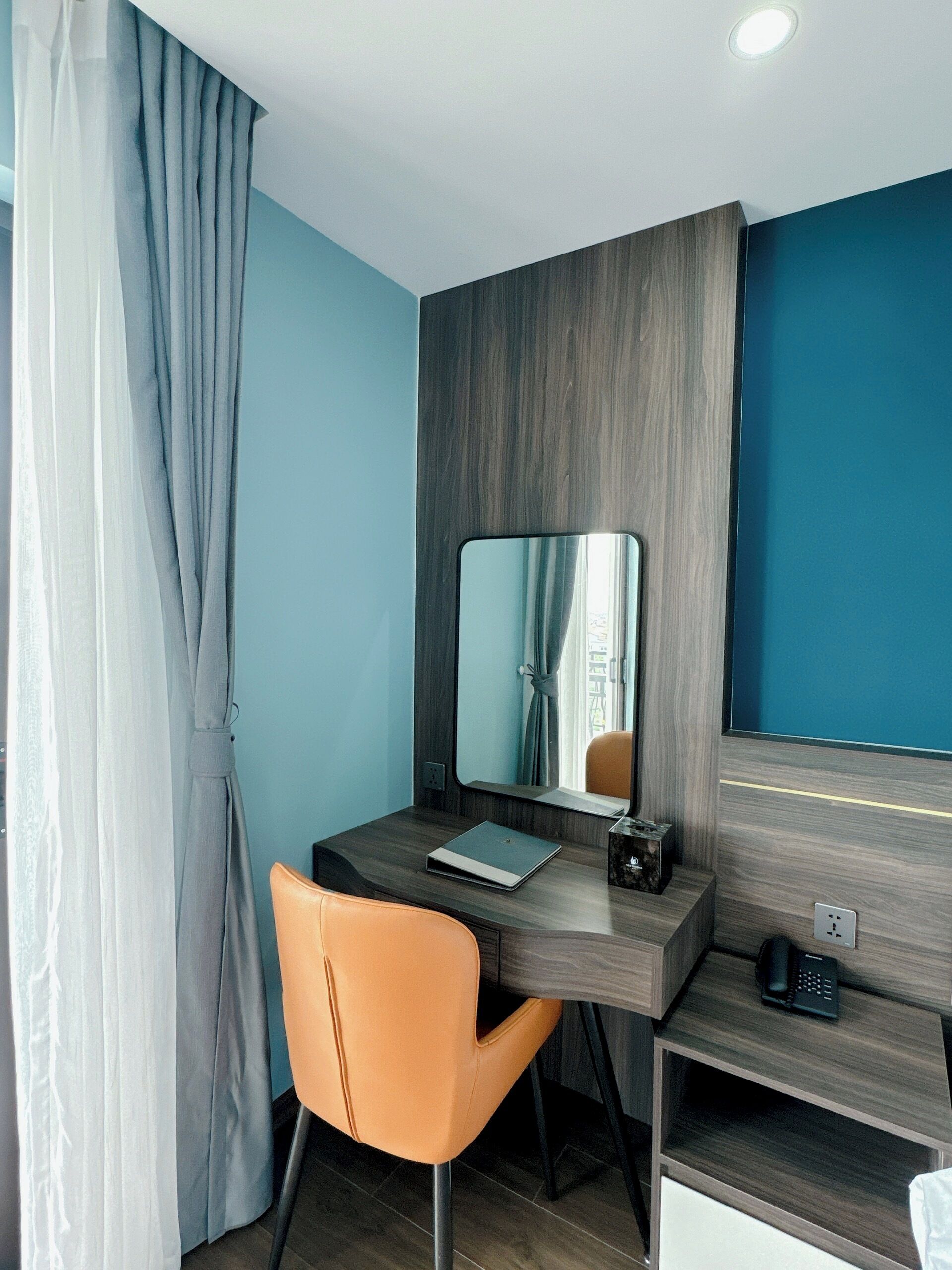 A modern room with a wooden desk, a laptop, a telephone, and a chair.