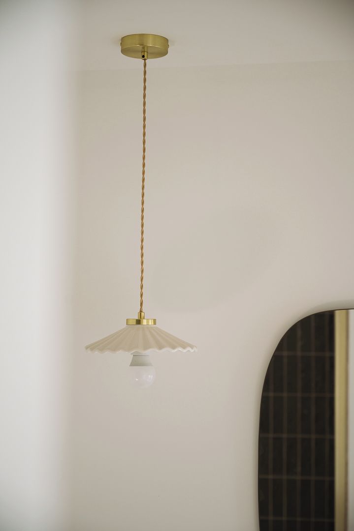 A pendant light fixture with a white shade and a gold-colored base, hanging from a ceiling with a braided cord.