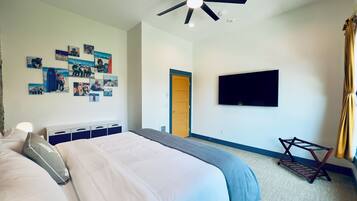 A bedroom with a bed, a ceiling fan, a mounted TV, and a door leading to another room.